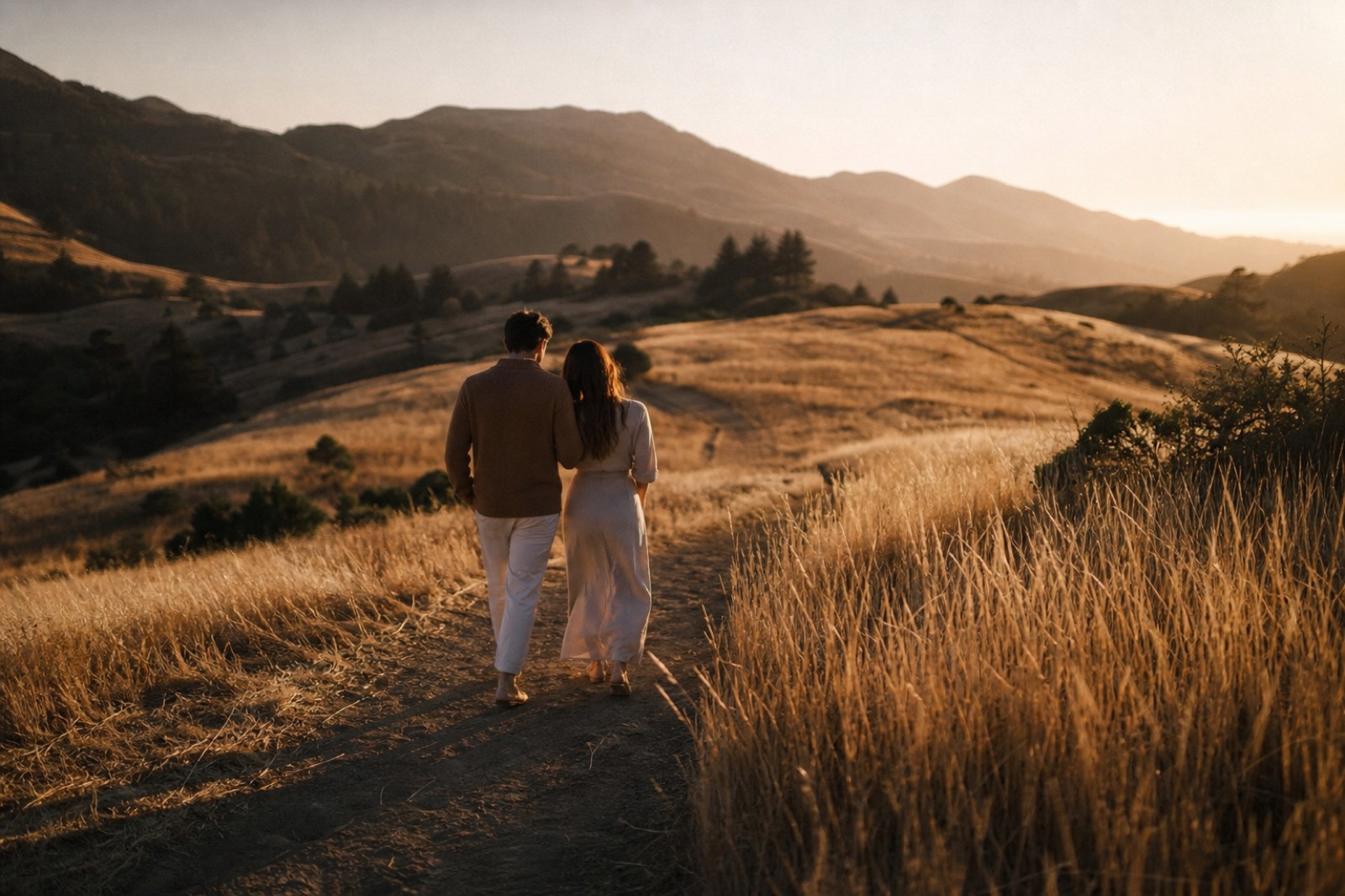 Two people walking together along a hillside path at sunset.