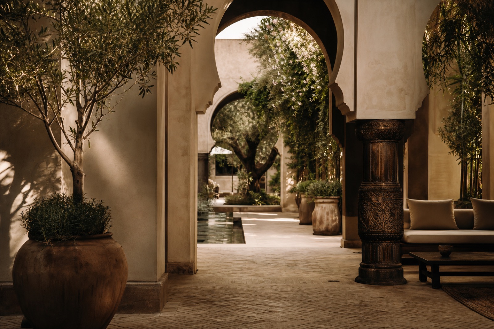 A sunlit courtyard framed by carved arches, with olive trees and potted plants.