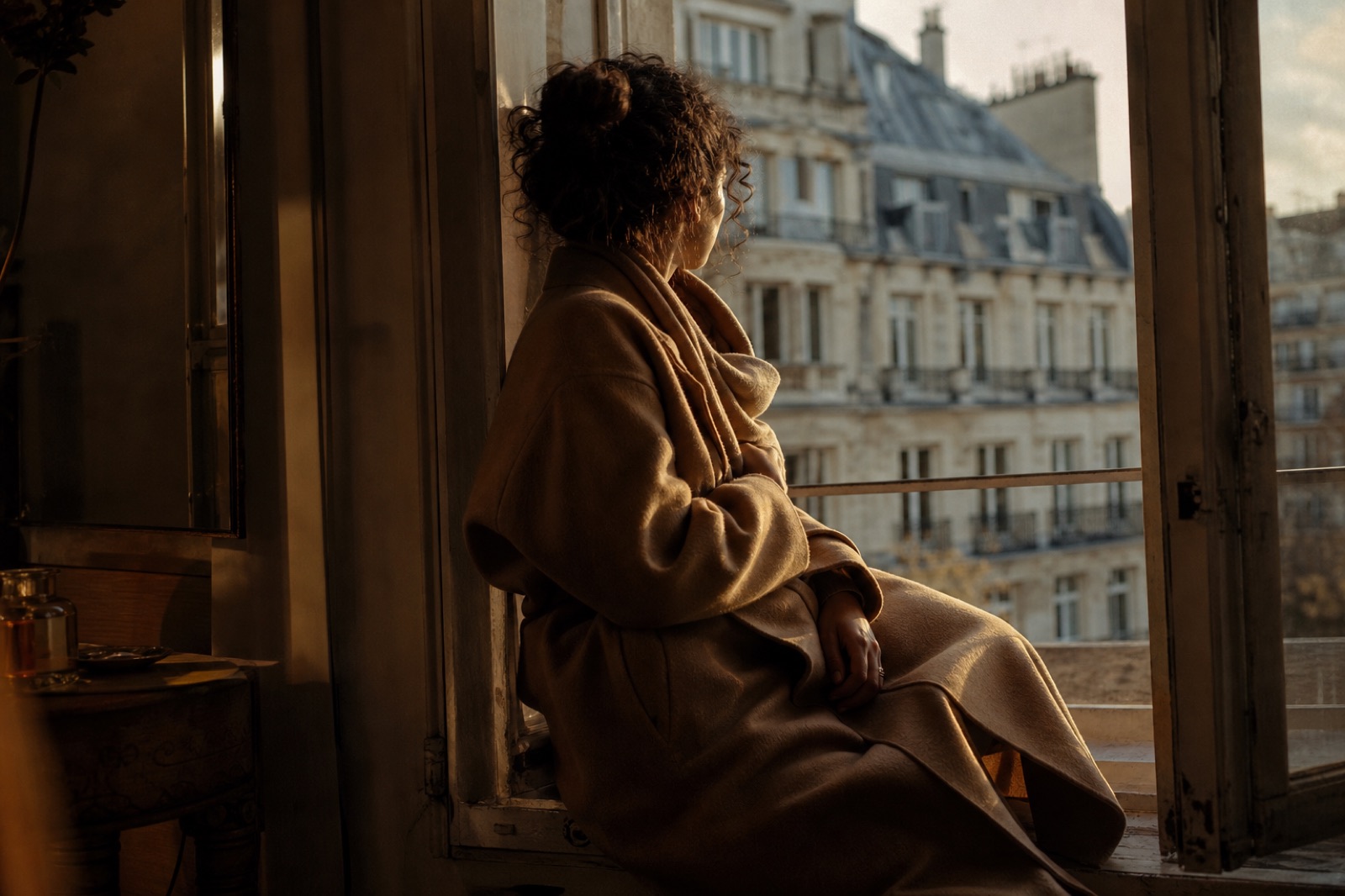 A person sitting by an open window, looking out over rooftops in the afternoon light.